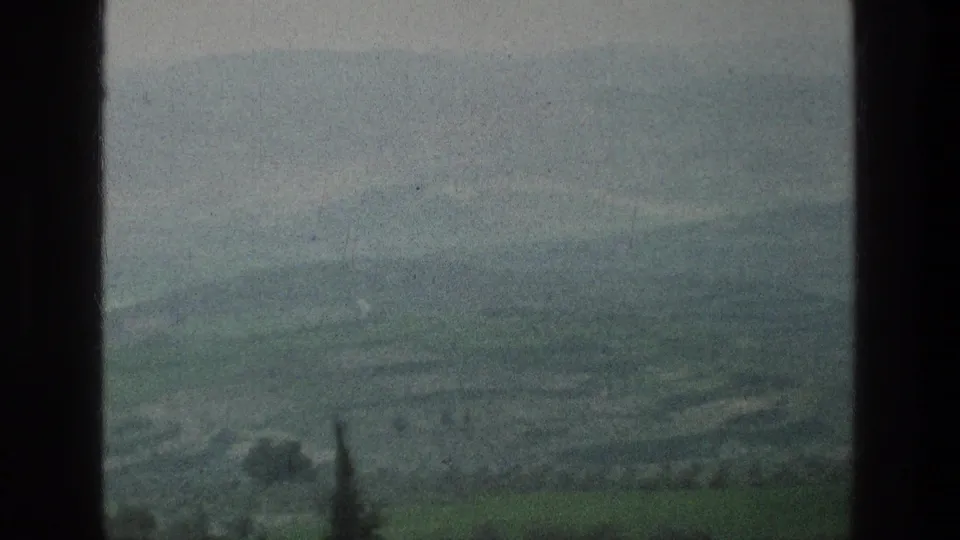 1976 8mm travel frame showing a hazy valley, green foreground, and distant terrain from the Jacobs Well Jerusalem metadata context.