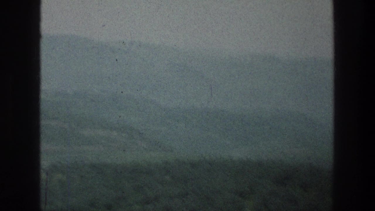 Soft, hazy hillside landscape with a dark vertical film edge at center.