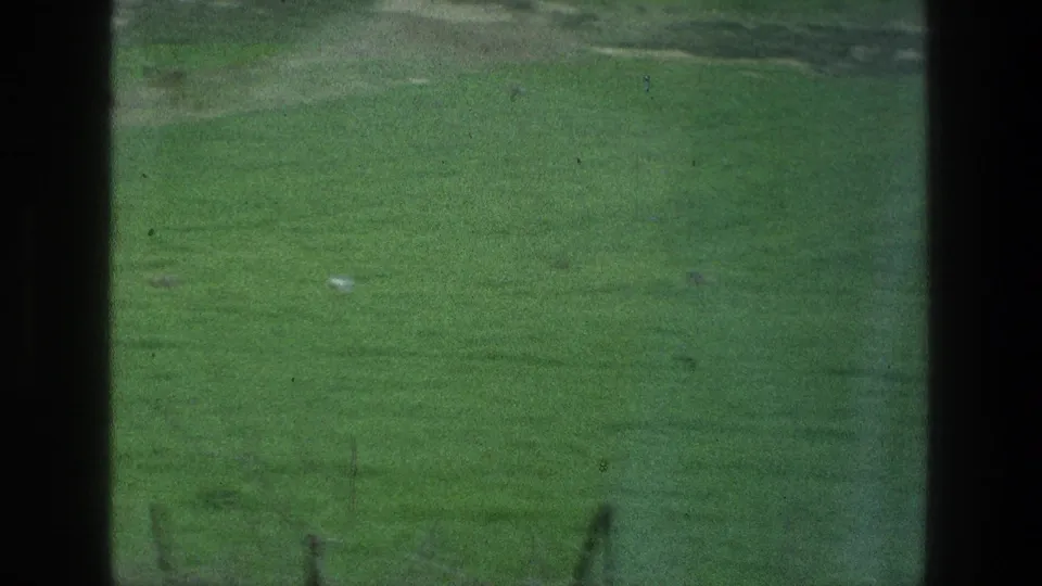 1976 8mm Jacobs Well Jerusalem Israel reel frame showing a green lawn, dark framing, faint posts, and a small white object.