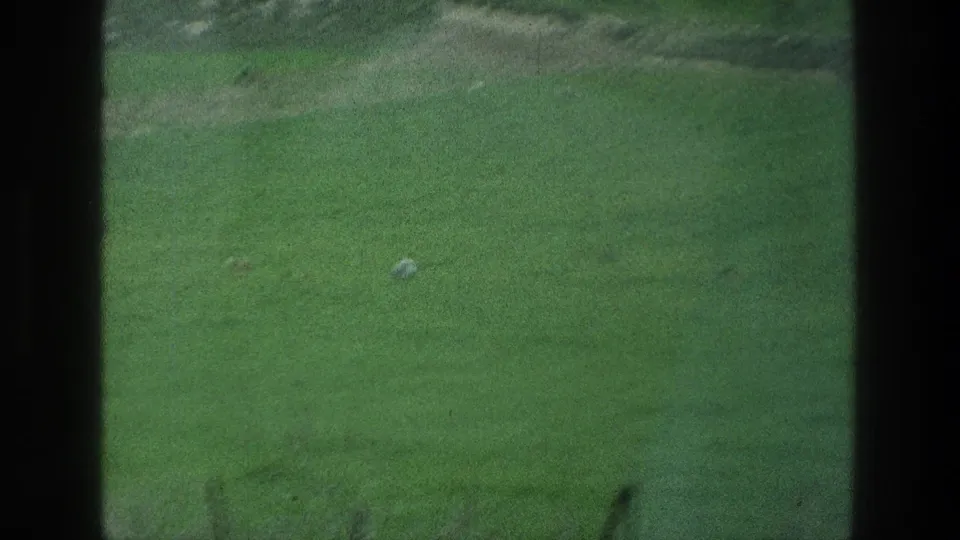 1976 8mm view of the Jacobs Well area in Jerusalem, showing a broad green field with a small pale ball-like object and dark frame borders.
