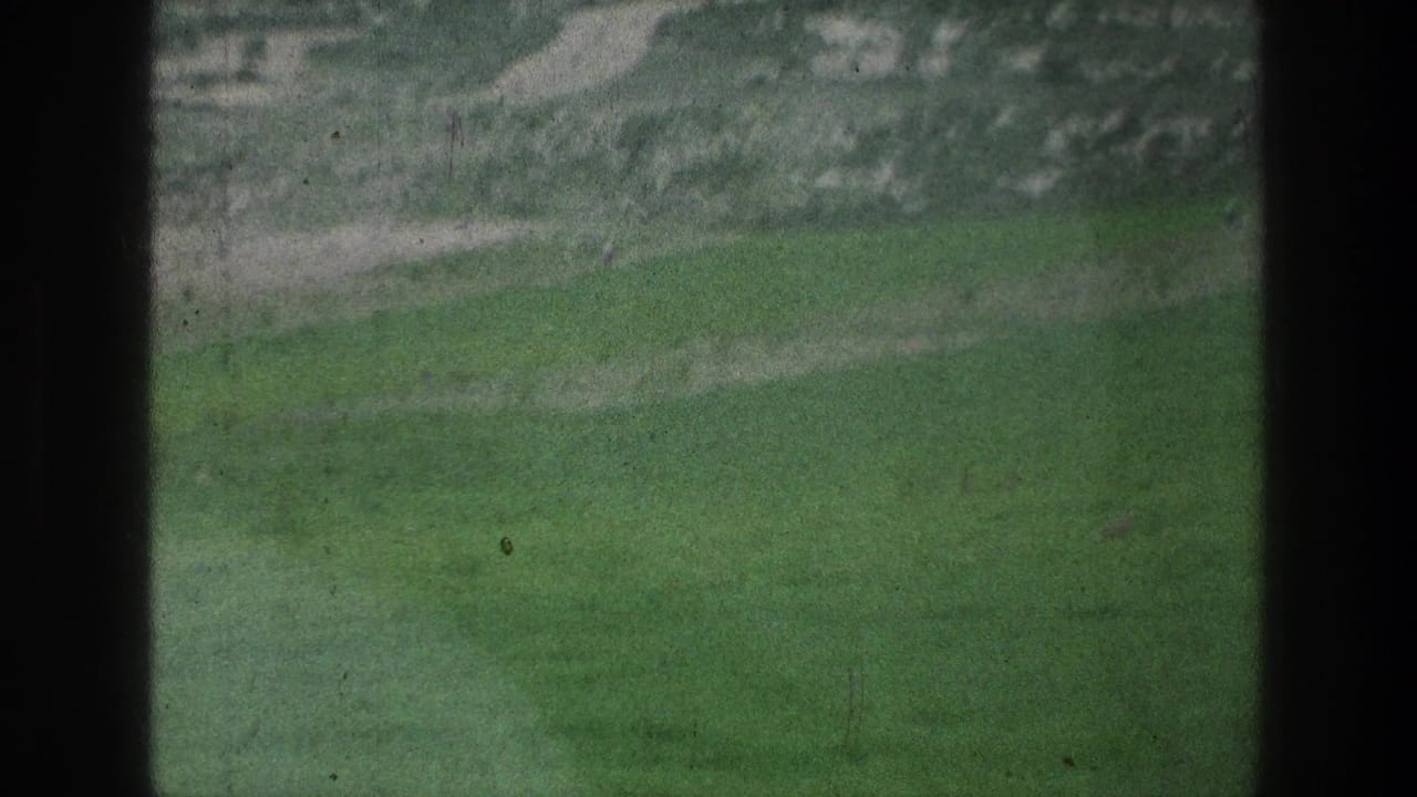 1976 8mm view of a grassy field near the described Jacobs Well, Jerusalem location, framed by dark vertical borders and soft focus.