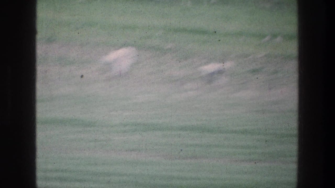 1976 8mm view near Jacobs Well, Jerusalem, showing a blurred green pasture with pale rocks and dark film-frame obstructions.