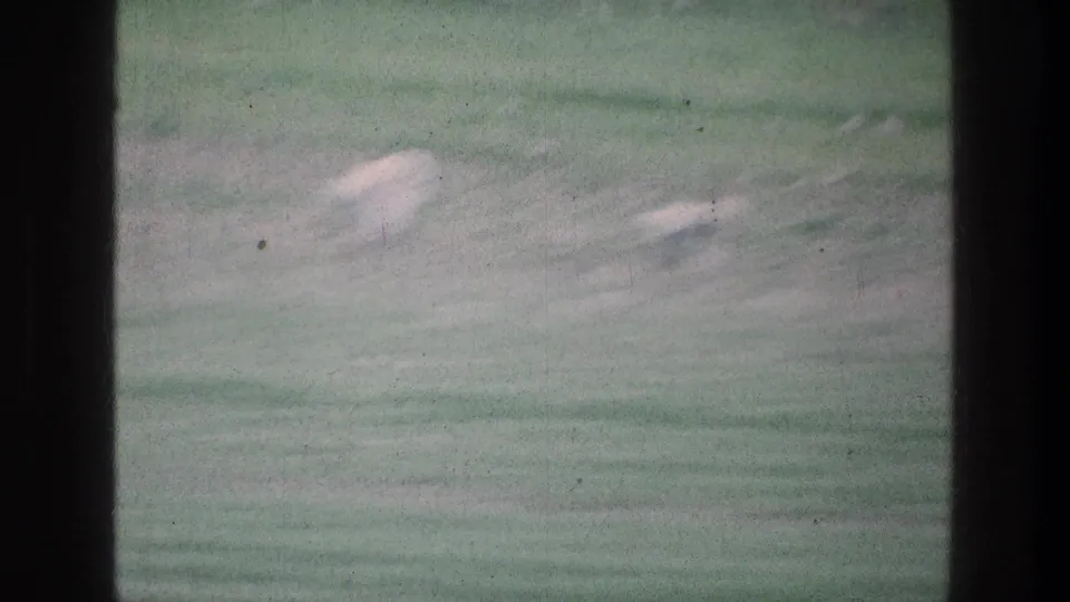 1976 8mm view near Jacobs Well, Jerusalem, showing a blurred green pasture with pale rocks and dark film-frame obstructions.