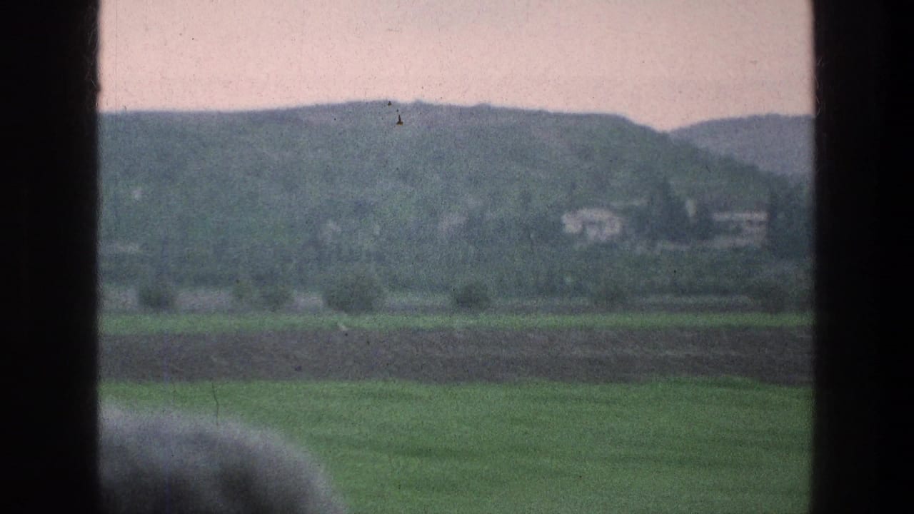 Green fields and distant hills viewed through dark train-window framing.
