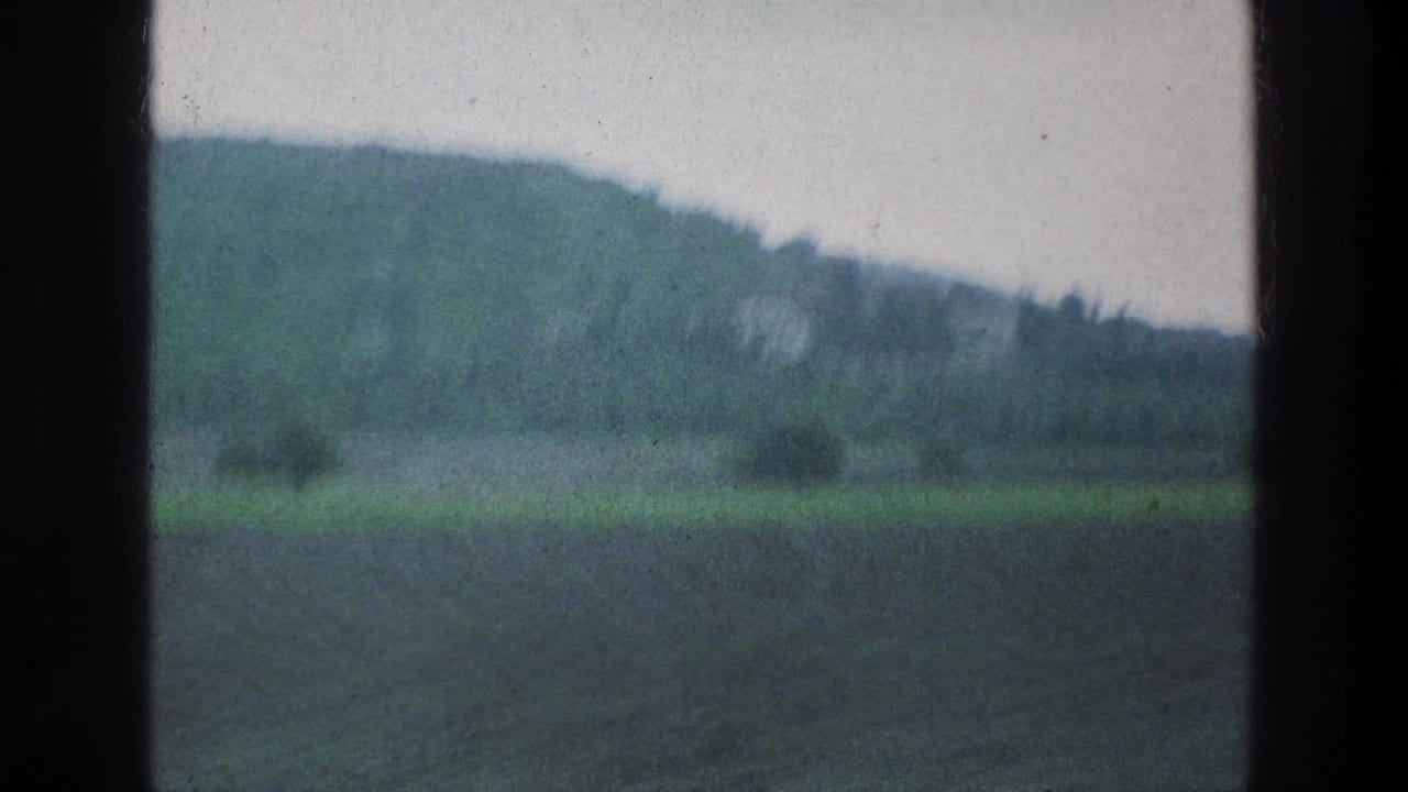 Distant hillside and field viewed through a vehicle window.