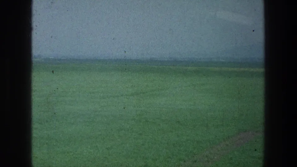 A soft, motion-blurred 8mm frame shows open green field and low horizon near the stated Jacobs Well Jerusalem area.
