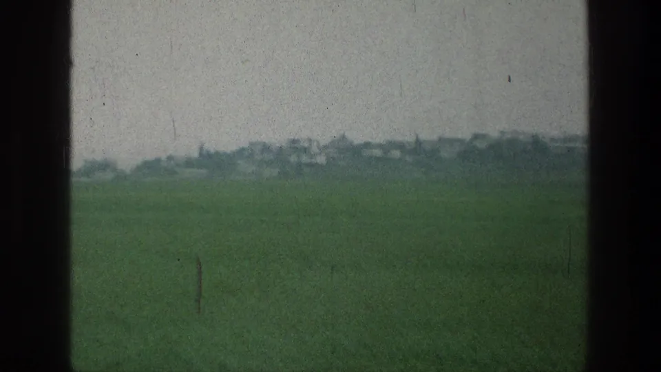 Green field near the stated Jerusalem-area location with distant low structures softened by haze and film grain.