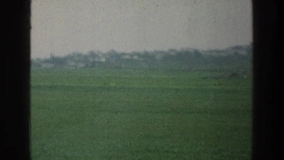 1976 8mm home-movie view of a green field near the cataloged Israel location, framed by dark vehicle or film-edge bars.