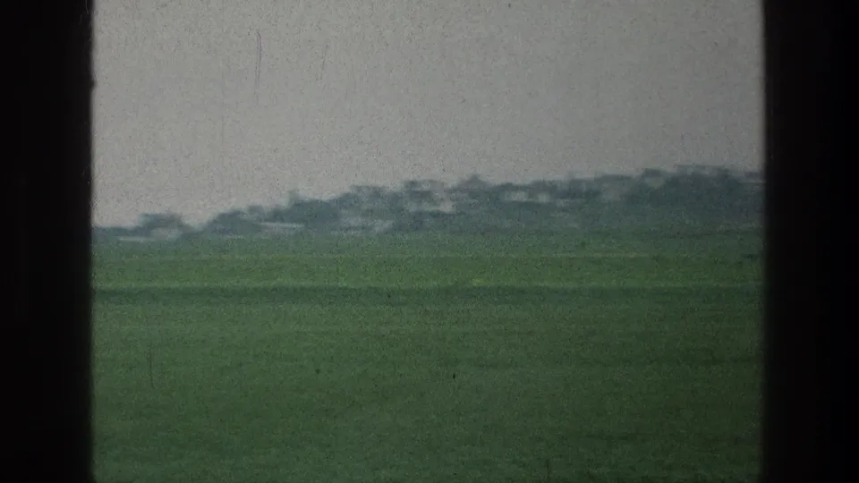 1976 8mm frame showing open green land near the cataloged Jerusalem area location, with distant low structures or trees softened by grain.