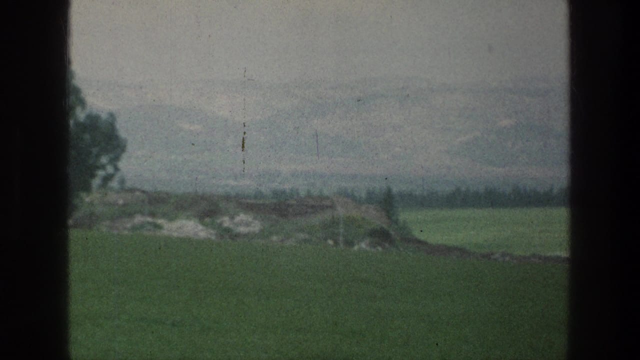 1976 8mm view associated with Jacobs Well Jerusalem, showing green fields, a low treeline, hazy hills, and dark window-like borders.