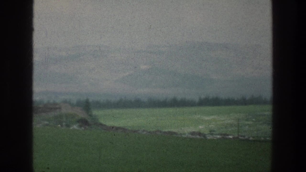Visitor-shot 8mm frame from the Jacobs Well Jerusalem metadata context, with open fields, hazy mountains, sparse trees, and dark side borders.