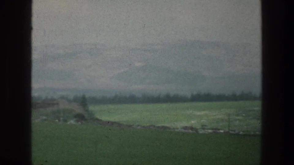 Visitor-shot 8mm frame from the Jacobs Well Jerusalem metadata context, with open fields, hazy mountains, sparse trees, and dark side borders.