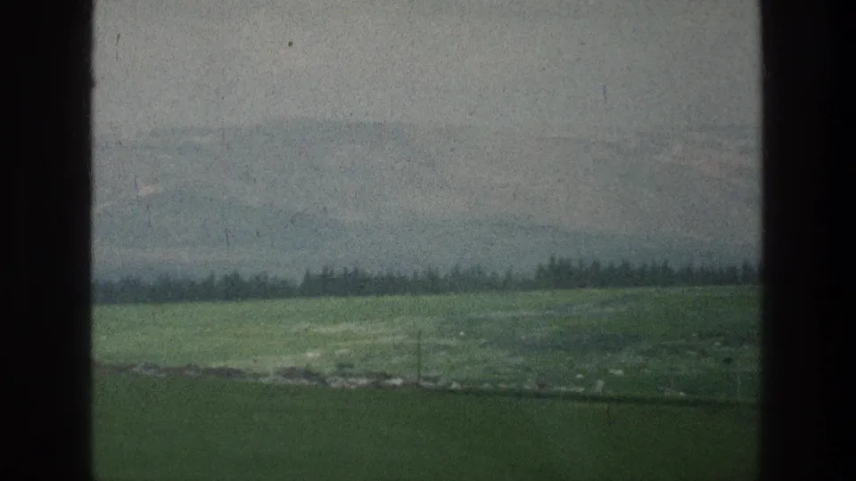 Green fields and a distant treeline appear beneath hazy hills in this 1976 8mm landscape frame associated with Jacobs Well Jerusalem.