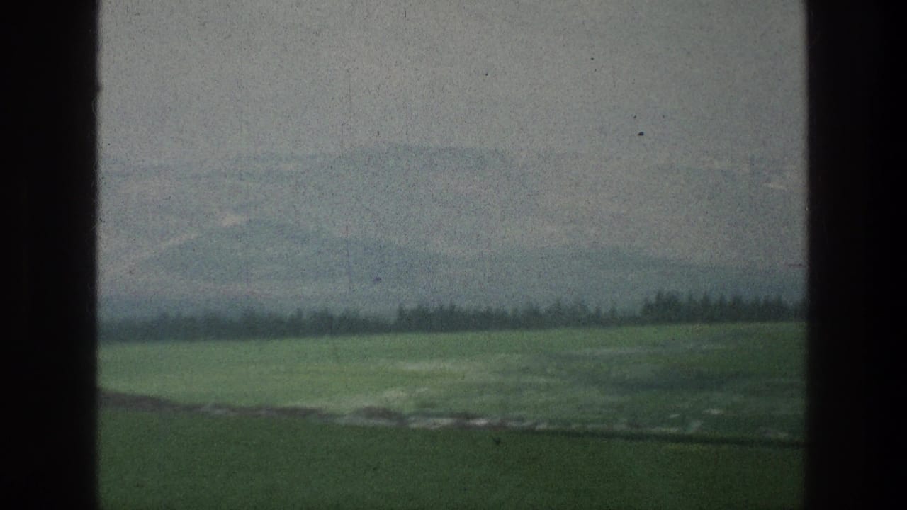 Green fields and hazy hills seen through dark window-like borders.