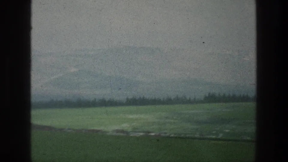 1976 8mm view of green countryside near the stated Jerusalem, Israel location, with hazy hills beyond dark vertical frame borders.