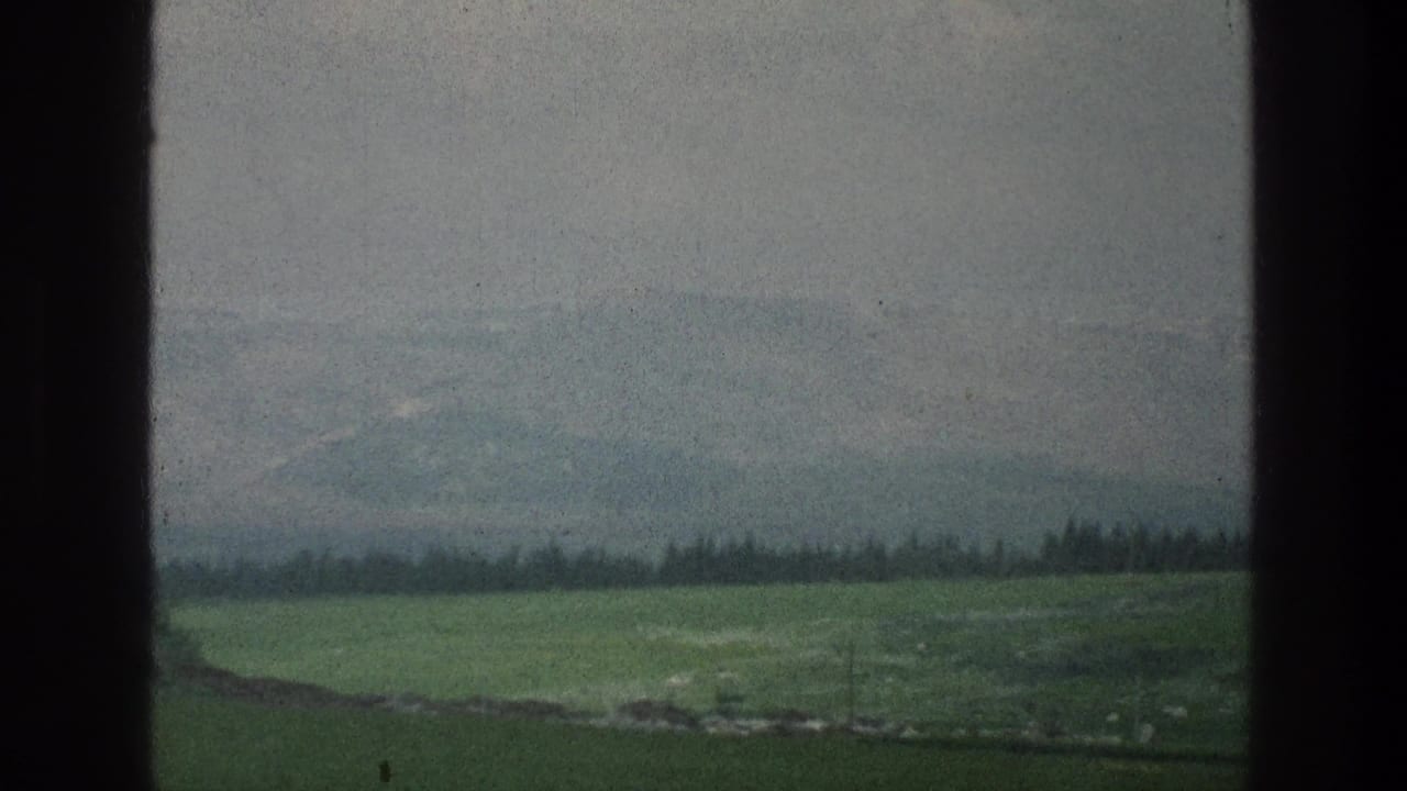 Rolling green fields, distant haze, and dark vertical borders across the frame.