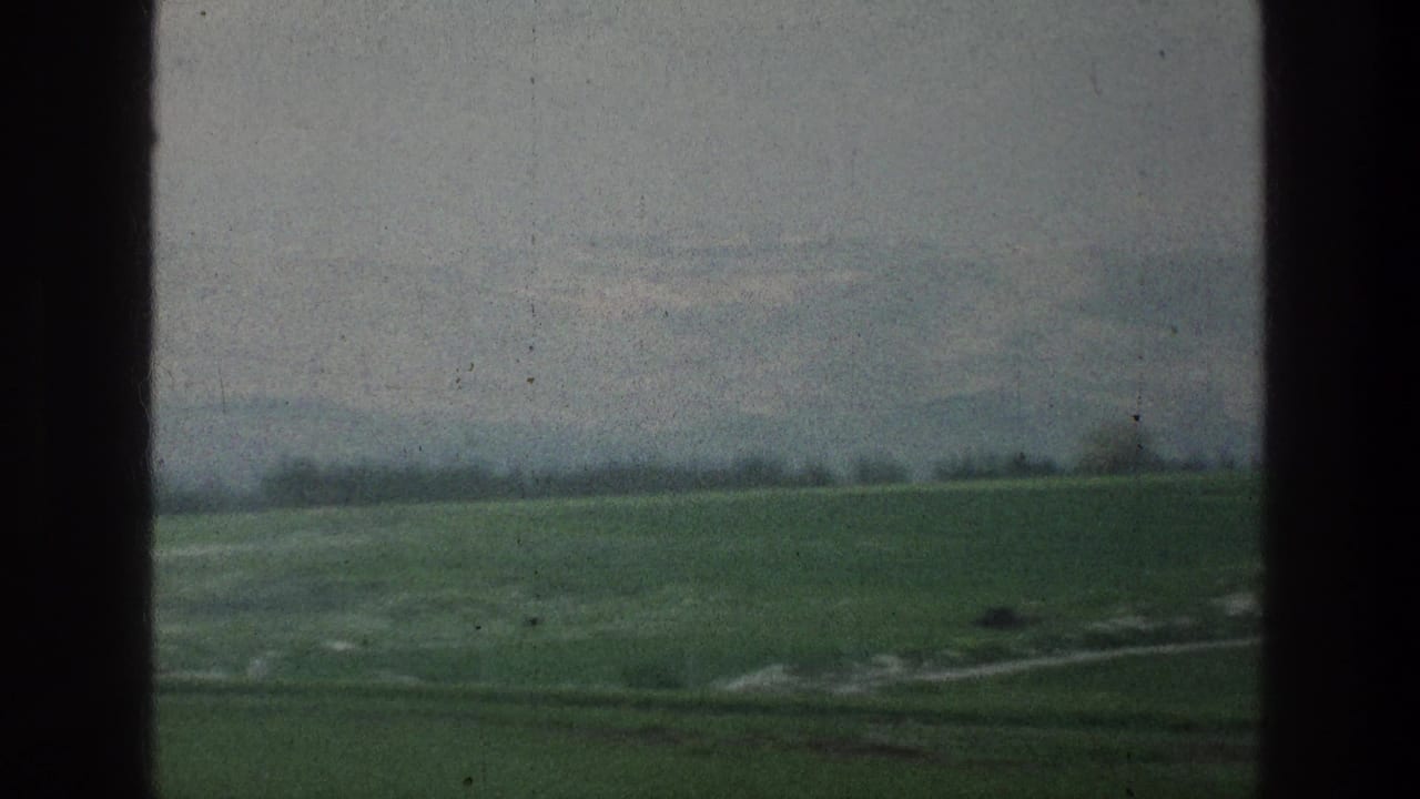 1976 8mm countryside view near Jacobs Well, Jerusalem, with green fields, a light path, and soft distant hills.