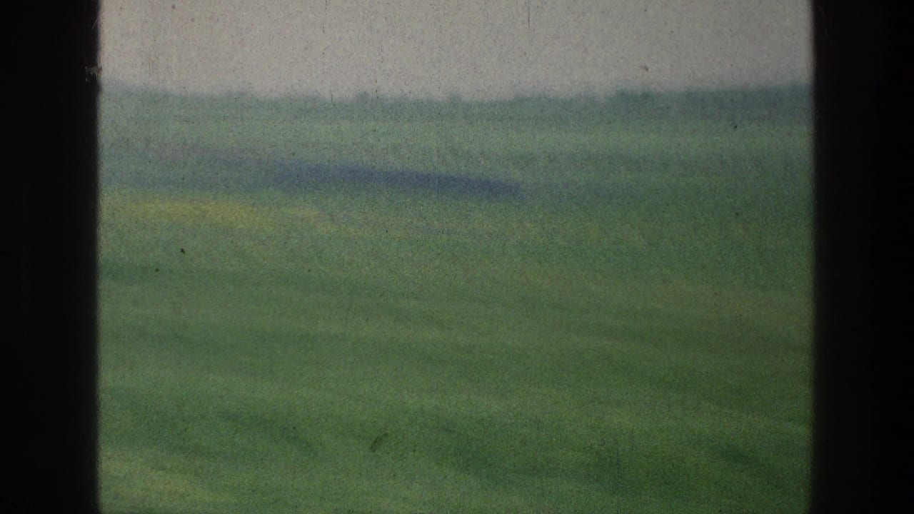 Green grassland and distant hazy hills seen between dark vehicle window edges.