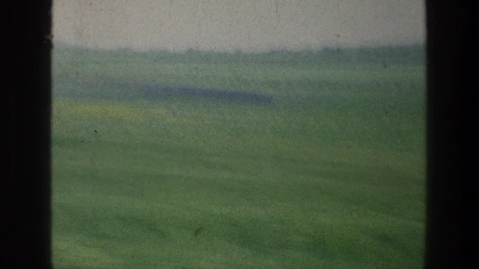 1976 8mm view in Israel of green fields and distant hills framed by dark vehicle-window edges.