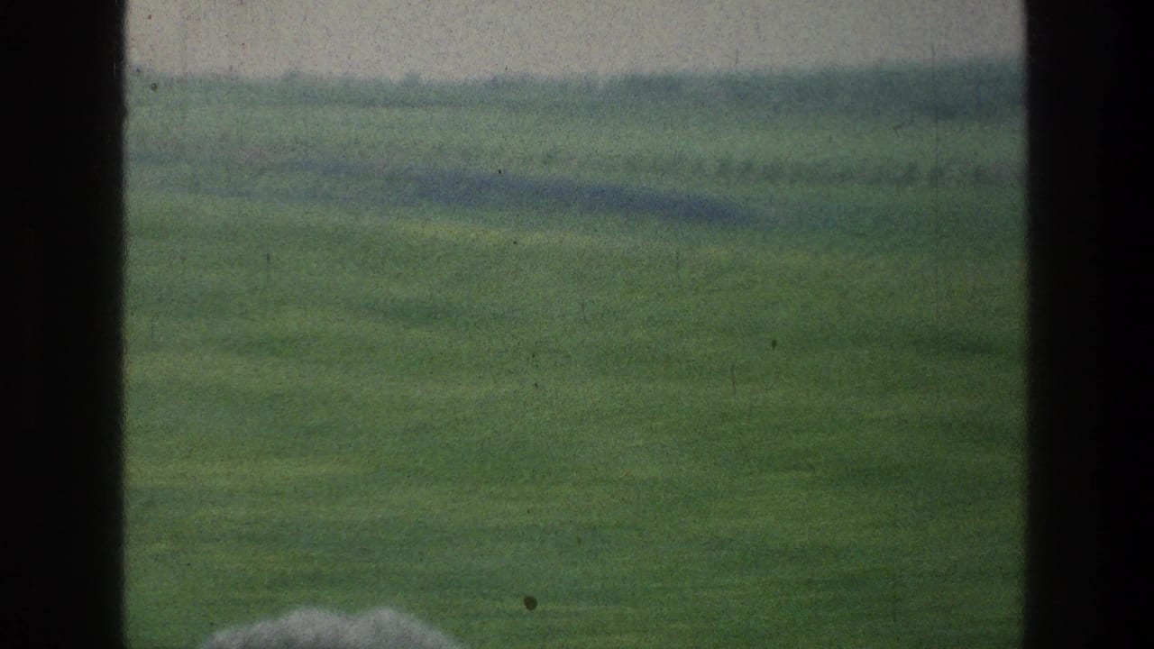 Hazy 1976 Israel landscape with grassland and distant hills partly blocked by a dark vehicle-window frame.
