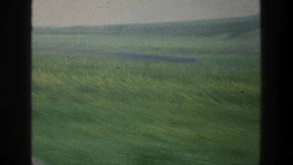 1976 home-movie frame showing rolling green fields in Israel with a hazy ridge beyond a vehicle window.
