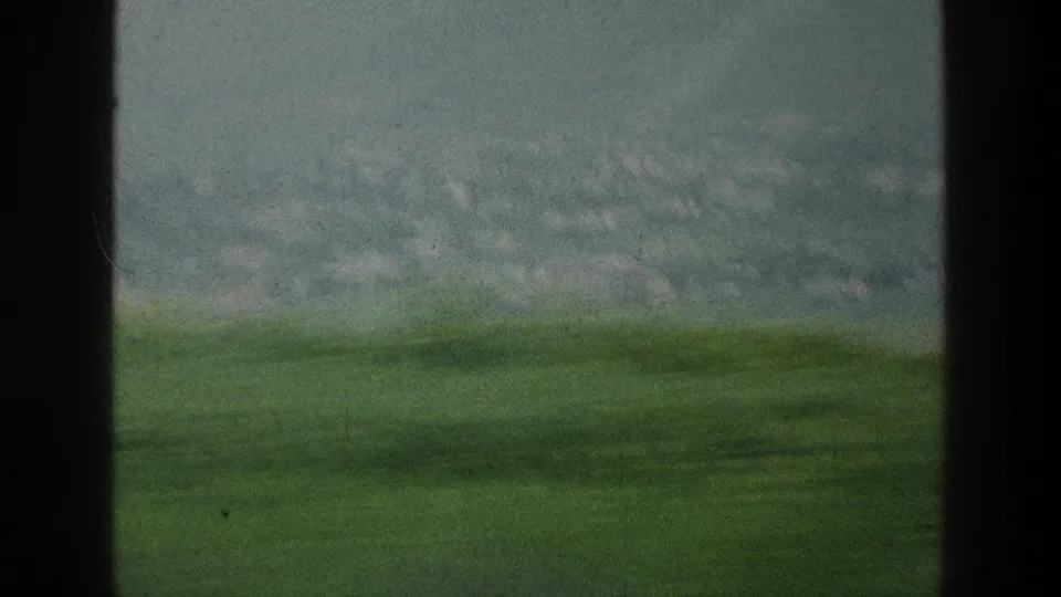 1976 8mm travel footage shows green rural terrain and a distant hill through the dark frame of a vehicle window.