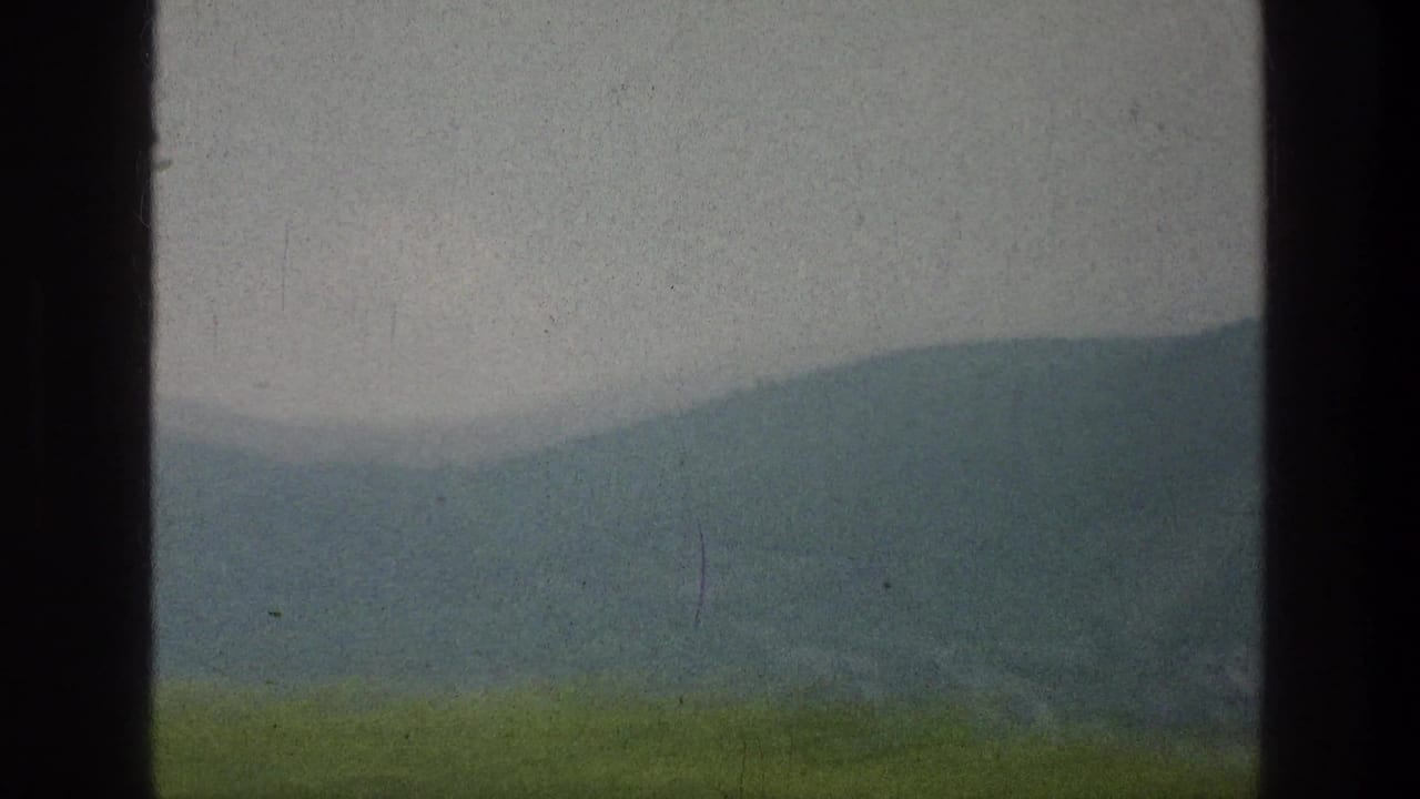 Distant blue-green mountain ridge viewed through a narrow vehicle window opening.