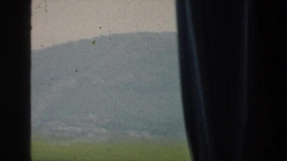 The vehicle view shifts across pale hills and green foreground, with a dark vertical window divider dominating the frame.