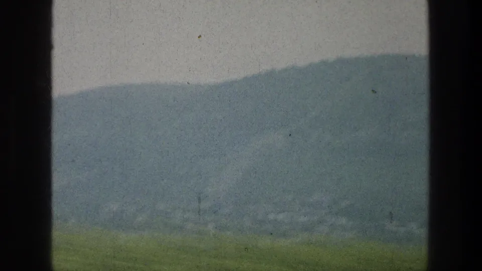 A soft, hazy mountain slope and green foreground remain visible through the vehicle window near the end of the short clip.
