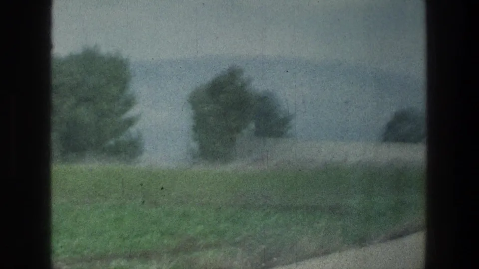 1976 8mm passenger view near Jacobs Well Jerusalem, with a blurred field, roadside edge, trees and hazy hills.
