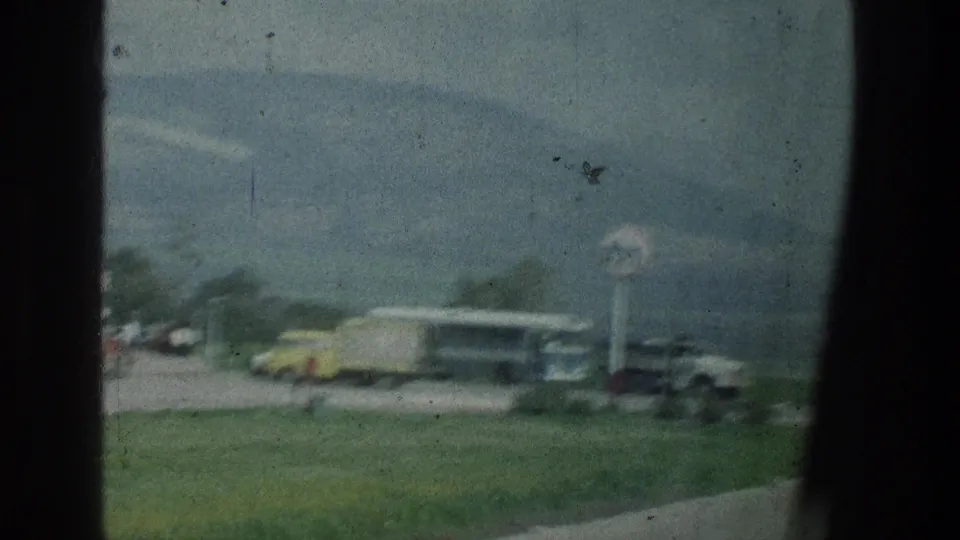 1976 8mm view of a roadside gas station area near the stated Jerusalem-area location, with a circular sign, bus, trucks, and mountains.
