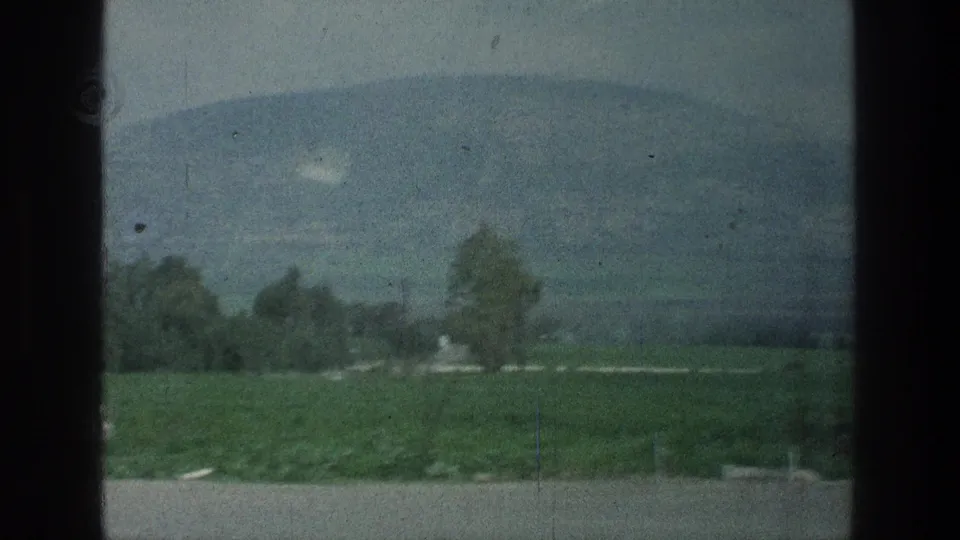 Passing 8mm view of green fields, scattered trees, roadside ground, and a broad mountain near the stated Jerusalem-area location.