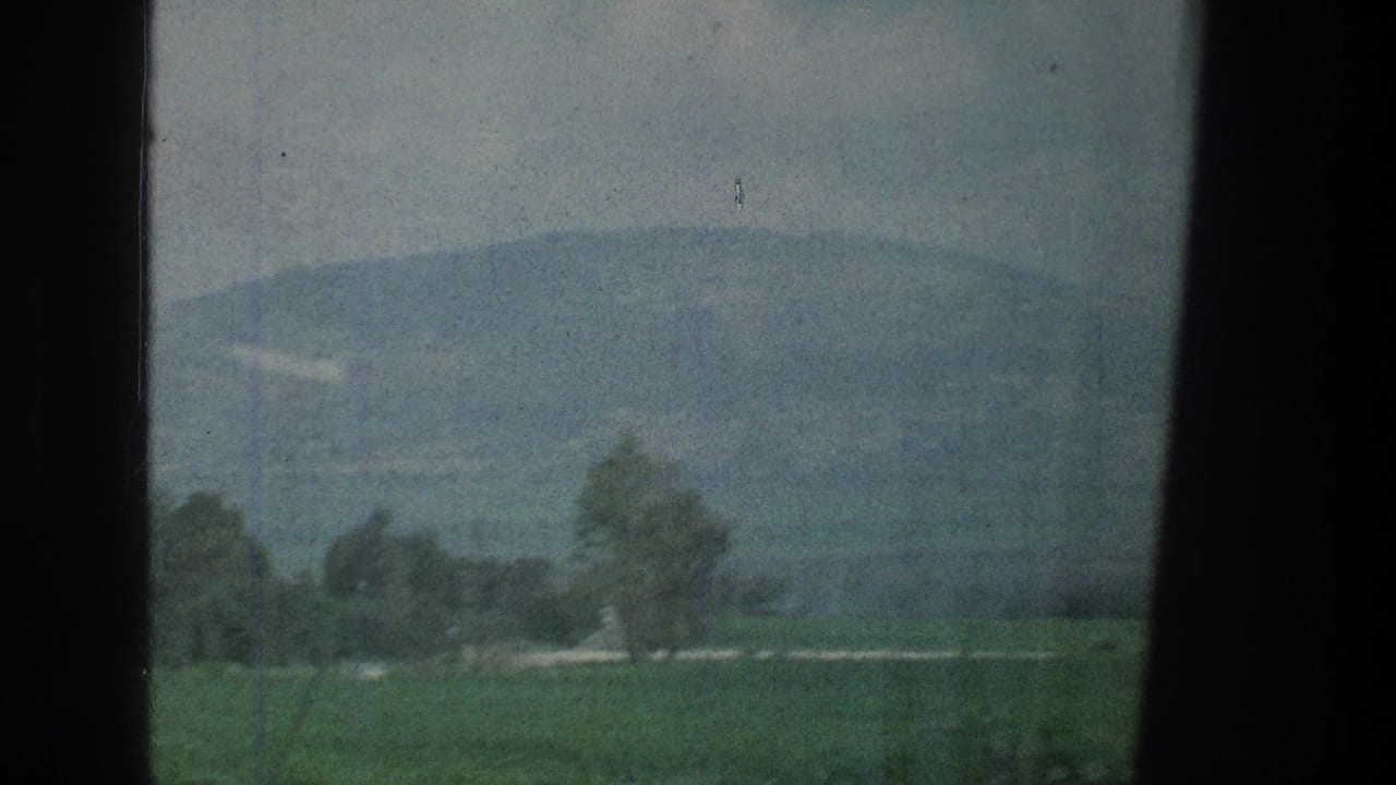 Hazy green fields and distant hills seen through a dark window frame.
