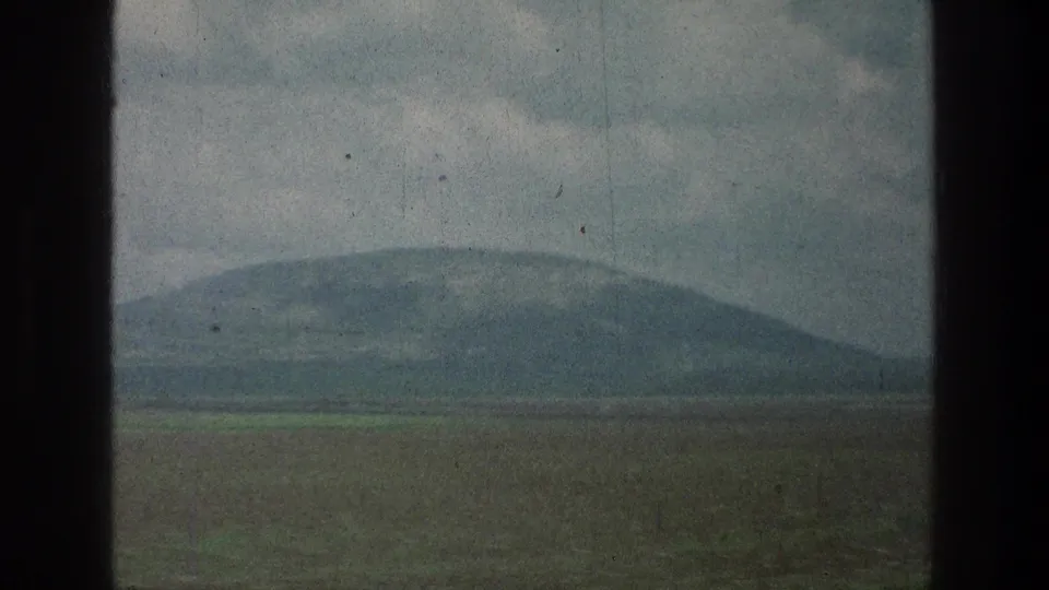 Window-framed 8mm view of flat fields and a low, hazy hillside, consistent with the cataloged 1976 Israel travel reel.