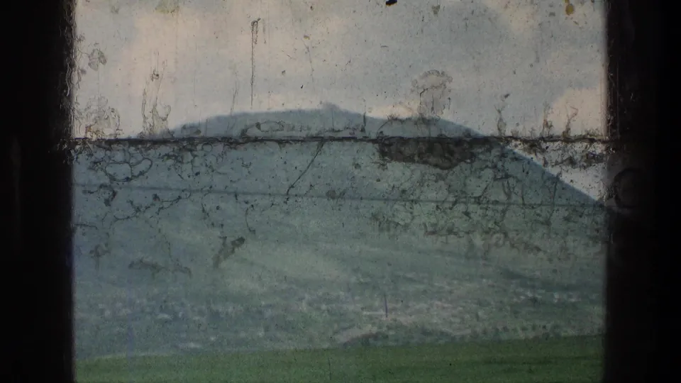 1976 8mm home-movie frame of a green hillside near the stated Jerusalem-area location, crossed by a power line and marked by film scratches.