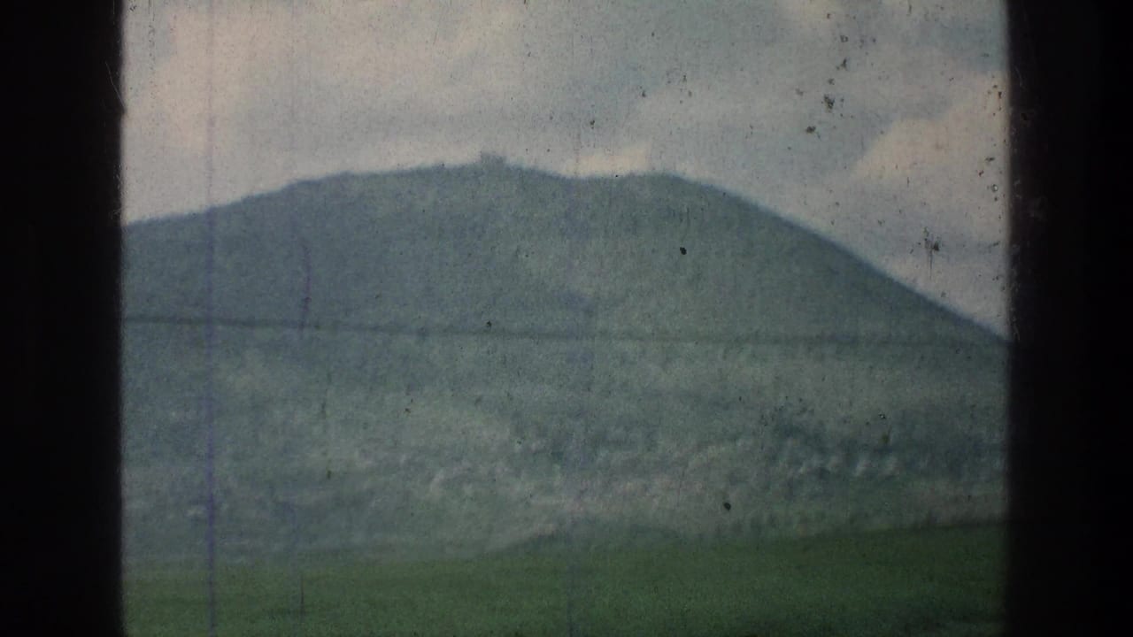 Rounded green hill beneath cloudy sky with a power line across the frame.