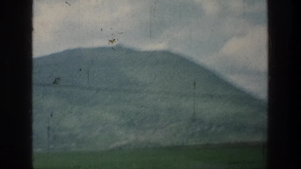 Final 1976 8mm frame of the Jerusalem-area landscape, showing a distant green hill, clouded sky, and power line through worn film texture.
