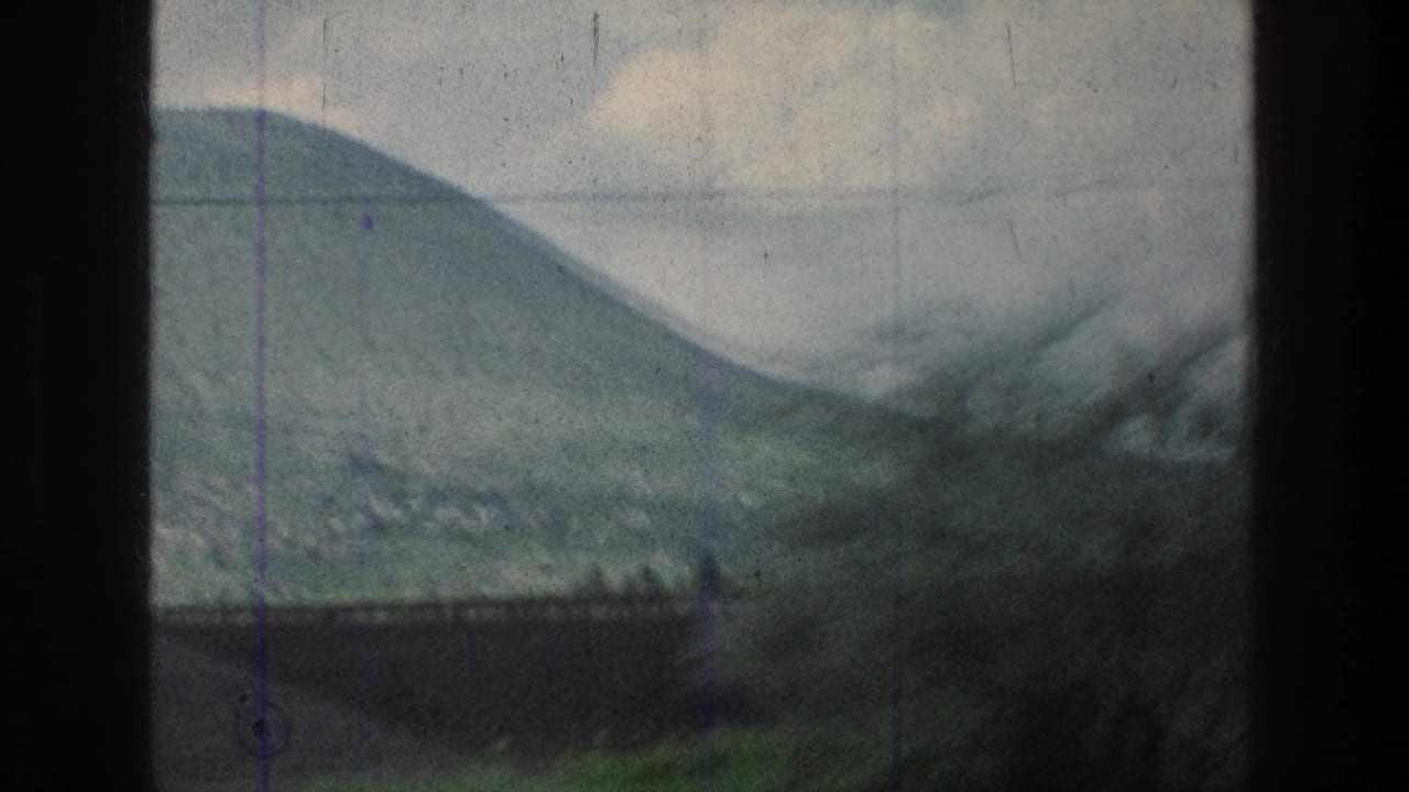 Moving 8mm vehicle view of a rounded hillside and roadside brush in the stated Jerusalem-area location, with utility wires crossing the sky.