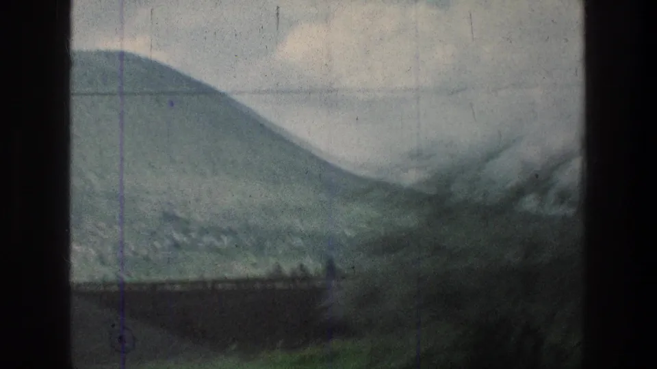 Moving 8mm vehicle view of a rounded hillside and roadside brush in the stated Jerusalem-area location, with utility wires crossing the sky.