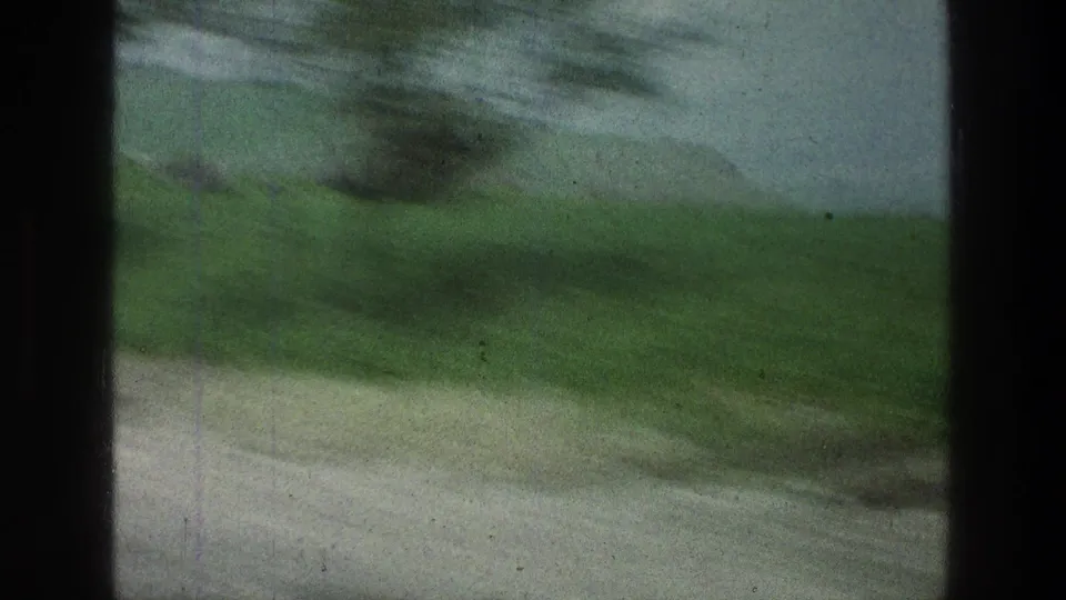 The final frame shows green hills and pale roadside ground blurred by vehicle movement, with dark window framing and visible 8mm film texture.