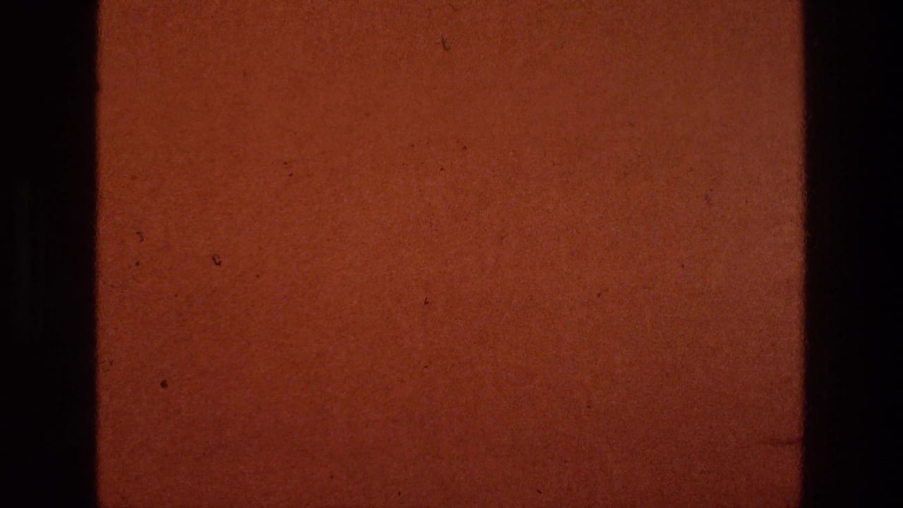A warm brown 8mm frame with dark gate edges, dust, and scratches appears between the roadside view and title card.