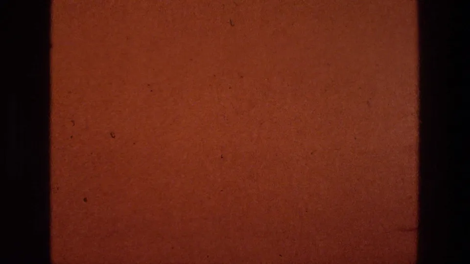 A warm brown 8mm frame with dark gate edges, dust, and scratches appears between the roadside view and title card.