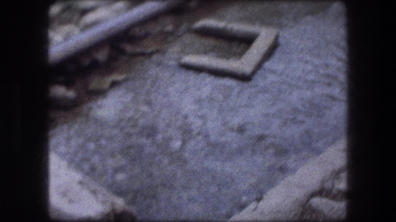 1976 Jericho 8mm view of a shallow murky stream beside rough concrete and stone banks.