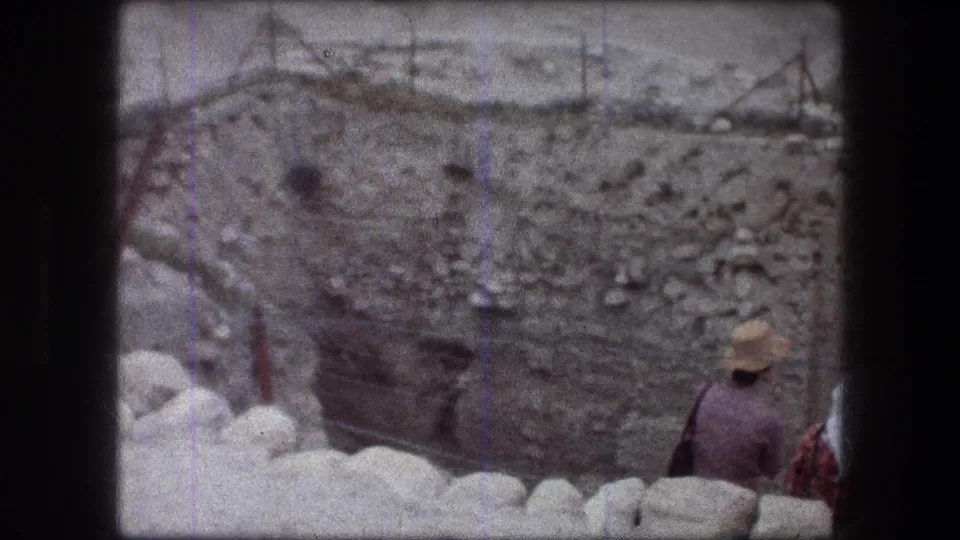 A 1976 home-movie frame shows a visitor near pale stones overlooking the Jericho excavation wall.