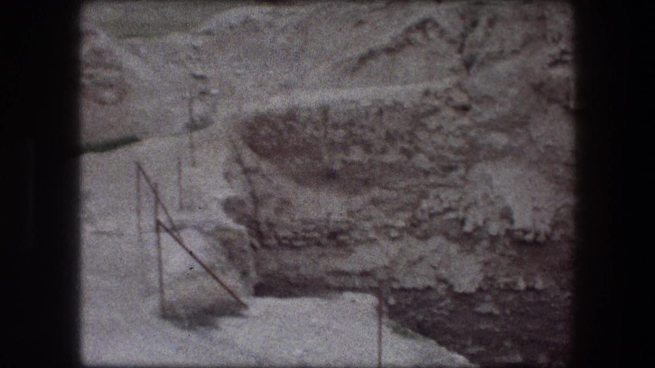 1976 Jericho 8mm frame showing rough rock or wall surface, pale ground, and a thin metal railing at the edge.