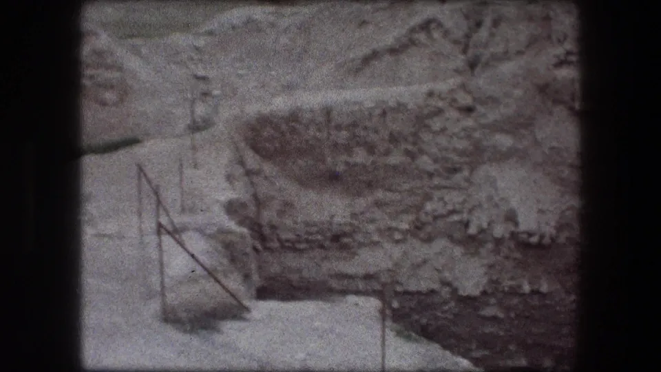 1976 Jericho 8mm frame showing rough rock or wall surface, pale ground, and a thin metal railing at the edge.