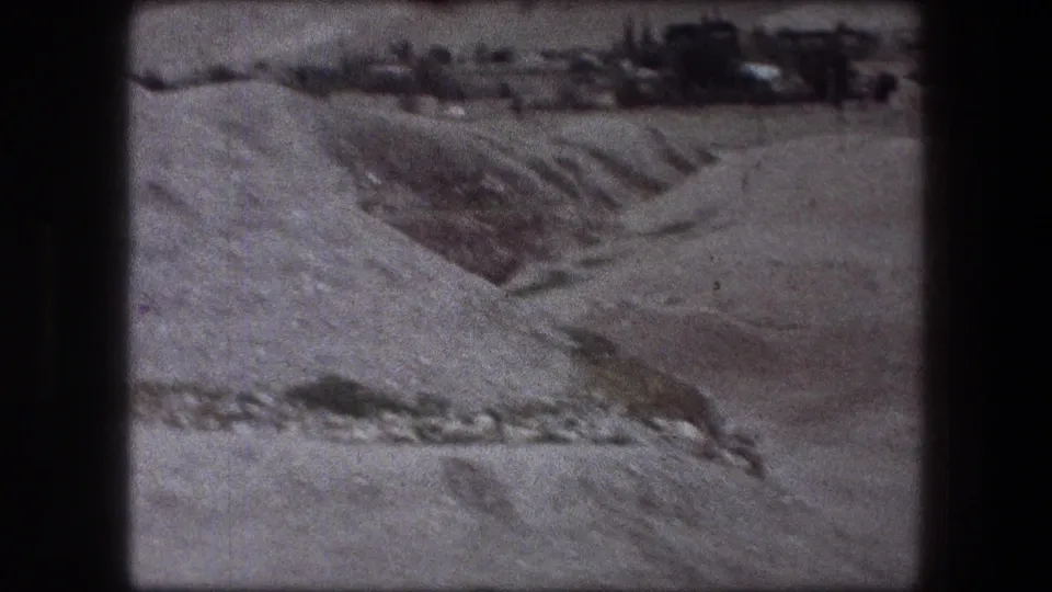 1976 Jericho 8mm frame showing a dry excavation slope, darker trench-like area, gravel surfaces, and distant rough terrain.