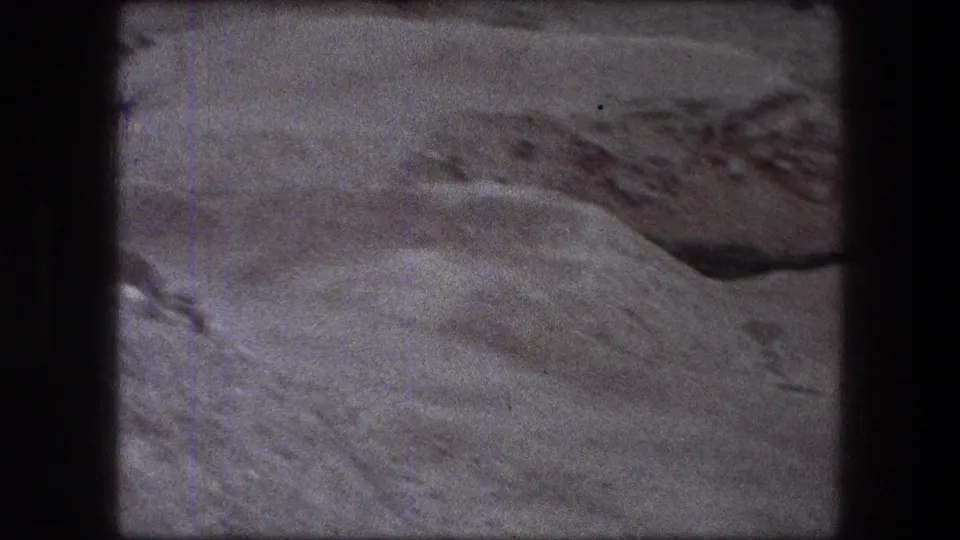 1976 Jericho 8mm frame showing pale uneven ground, a dark hollow or cut, and rough excavated earth along the upper edge.