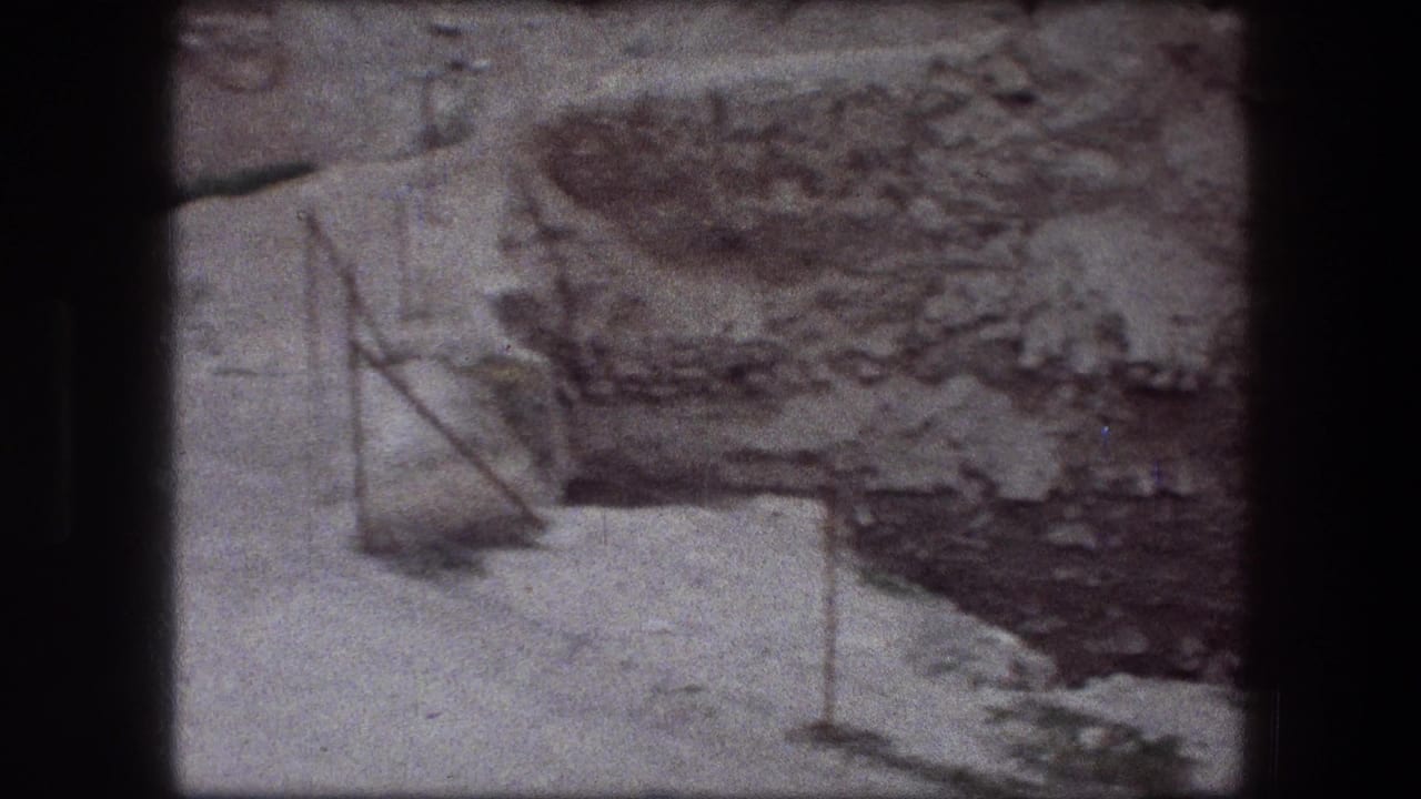 Rocky pit edge with pale ground, metal posts, and rough stone layers.