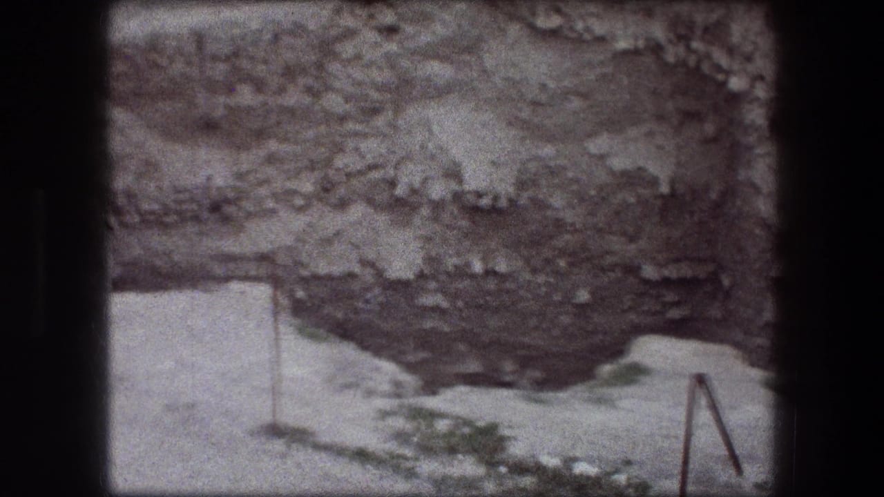 Rocky pit wall with a pale path, sparse greenery, and a metal railing at the edge.